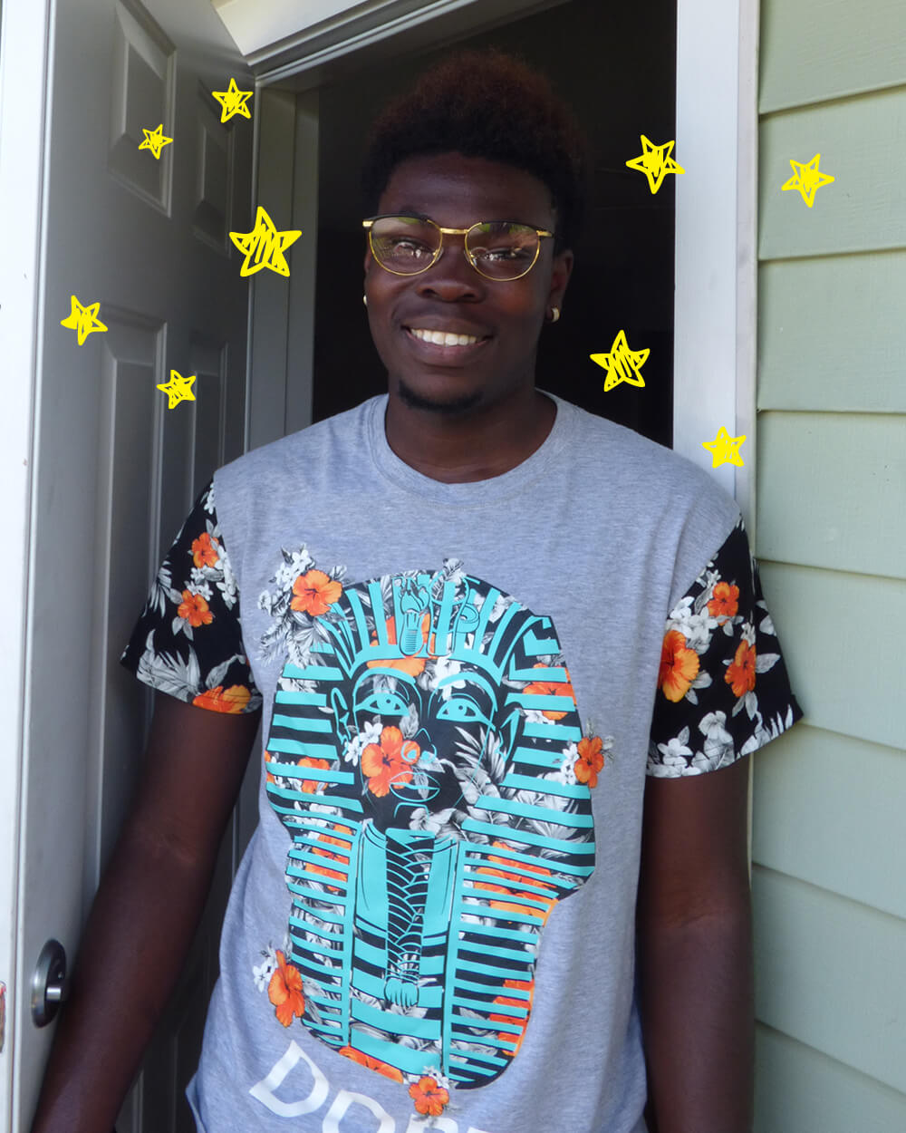 Young man with glasses smiling outside, wearing a graphic T-shirt and floral sleeves.
