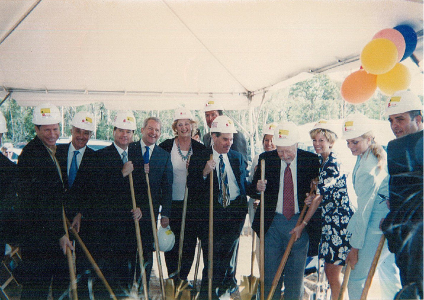 Group of professionals at groundbreaking event with shovels and safety helmets.